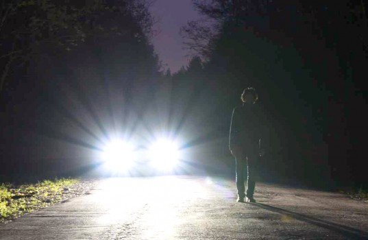 car-headlights-shining-at-night-with-man-standing-on-the-road