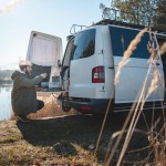 Junger Mann mit umgebautem Camper-Van am See