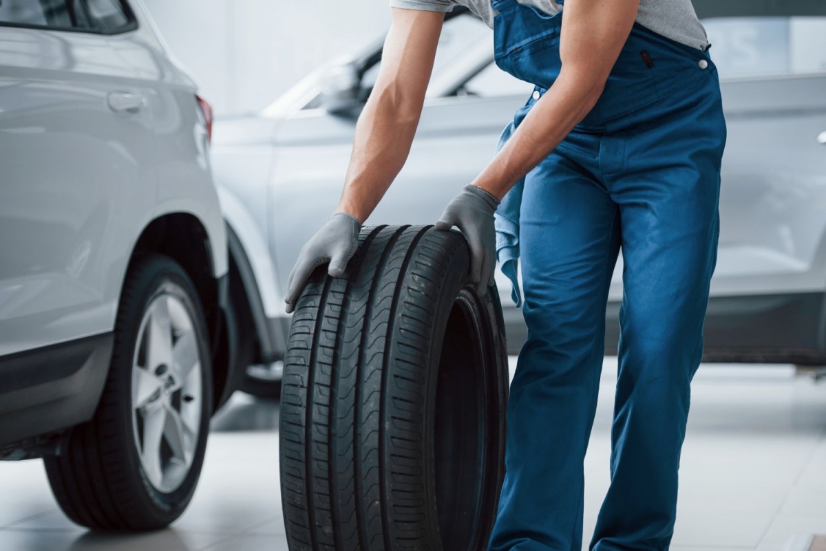 On my way. Mechanic holding a tire at the repair garage. Replacement of winter and summer tires